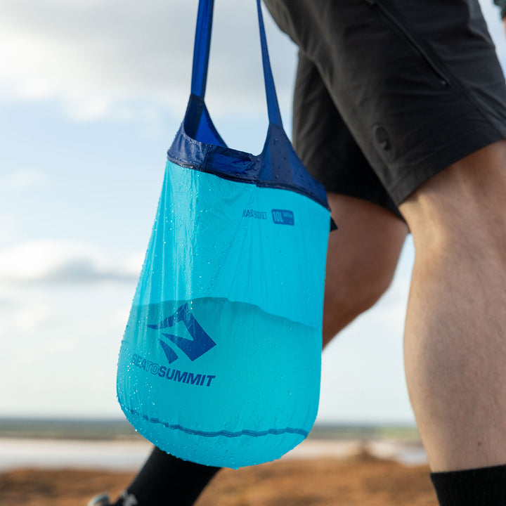 Person carrying a collapsible nylon bucket of water in the outdoors.