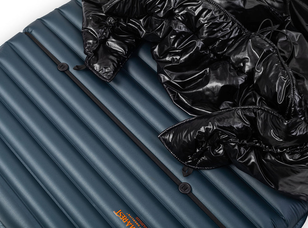 A black quilted puffer sleeping quilt shown against a navy blue sleeping pad