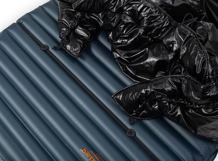 A black quilted puffer sleeping quilt shown against a navy blue sleeping pad