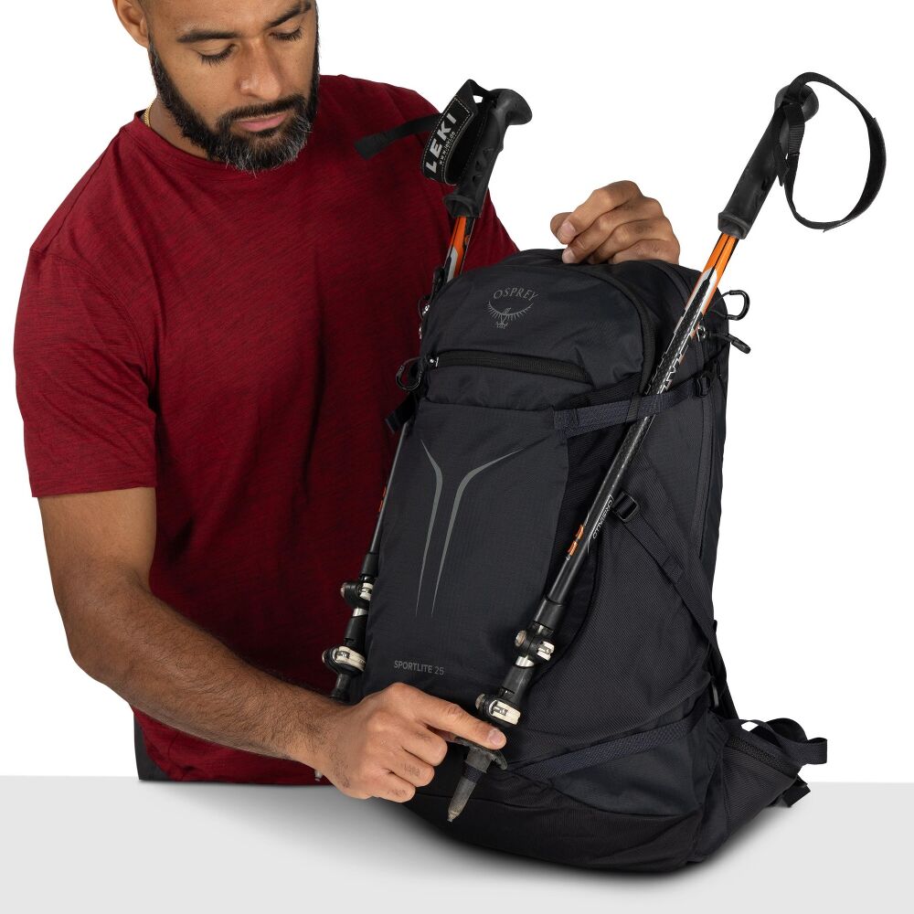 Man adjusting a black Osprey backpack with hiking poles on a white background