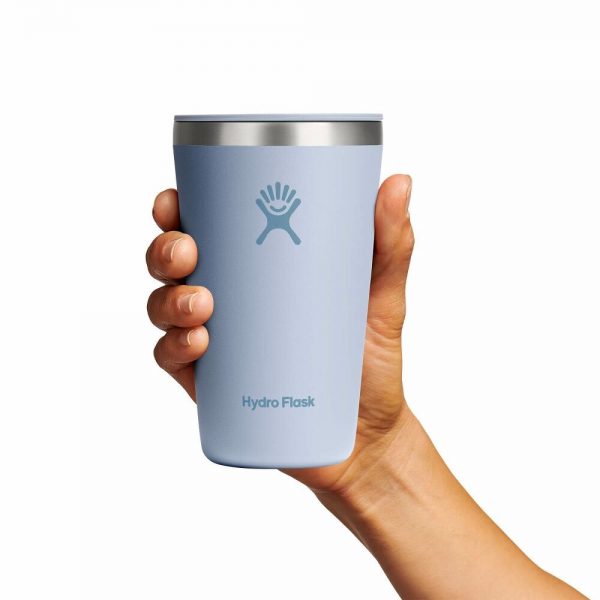 A hand holding a light blue Hydro Flask tumbler with a stainless steel lid against a plain white background.