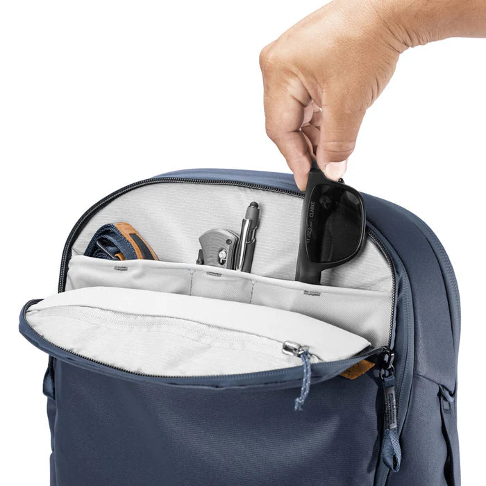 Hand placing sunglasses into a blue backpack with compartments.