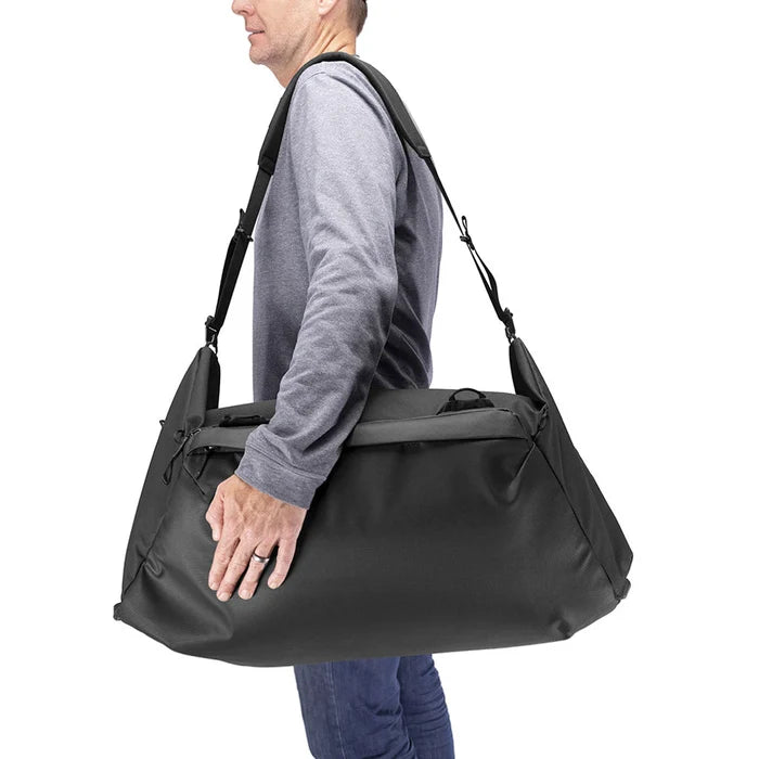 Person carrying a large black duffel bag on a white background