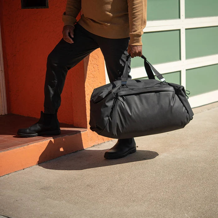 Person holding a black duffel bag against a colorful wall.