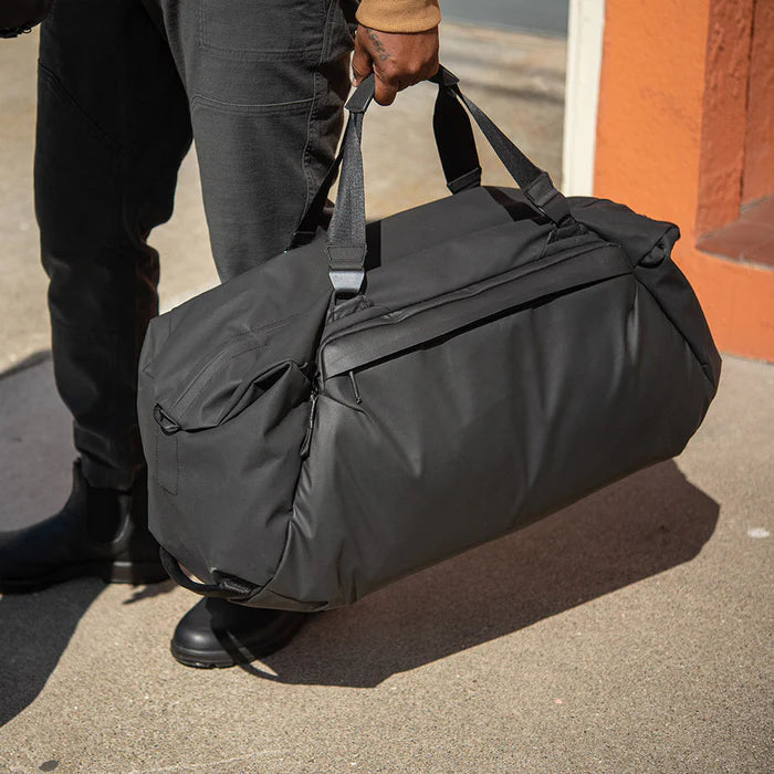 Person holding a black duffel bag on a sidewalk