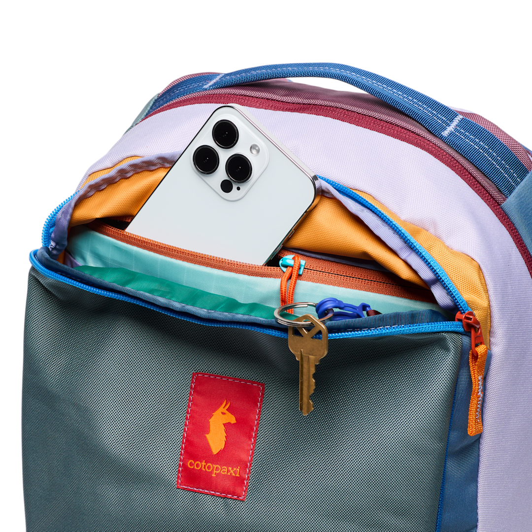 Open backpack with phone, wallet, and key, featuring Cotopaxi brand logo.