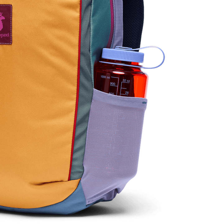 Red water bottle in a pocket of a yellow backpack with a white background