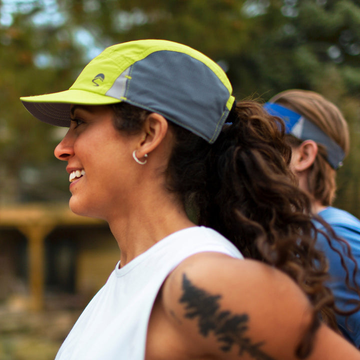 Woman wearing a green and grey cap outdoors with another person in the background.