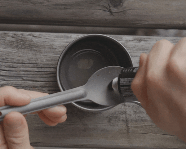 Hands holding a pork over a cup and squeezing coffee paste onto spork