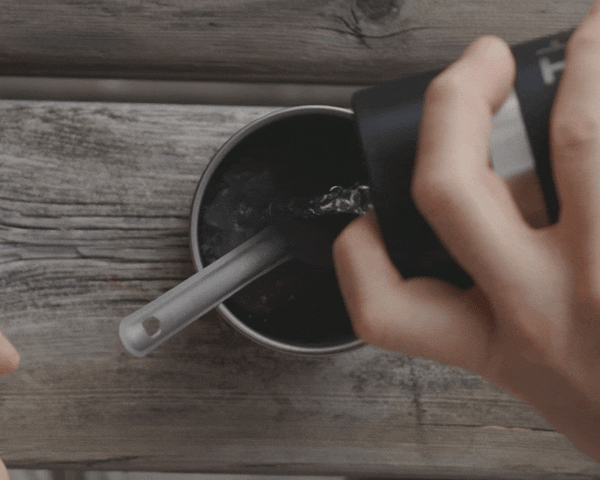 Someone pouring water into a cup with spork and coffee paste.
