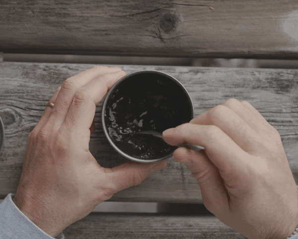 Someone stirring a spork in a cup that is filled with coffee